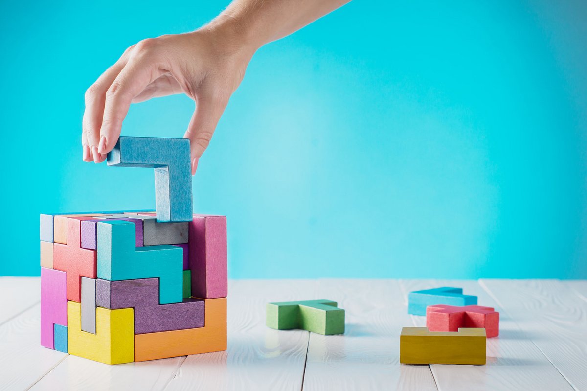 Eine Hand setzt ein farbiges Holzbaustein-Element in ein Puzzle ein