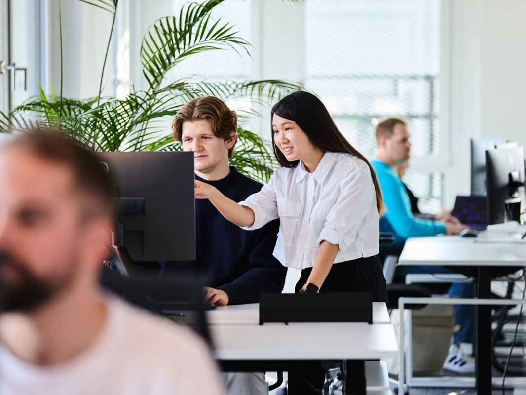 Zwei junge Mitarbeitende schauen gemeinsam auf einen Bildschirm in einem hellen Büro