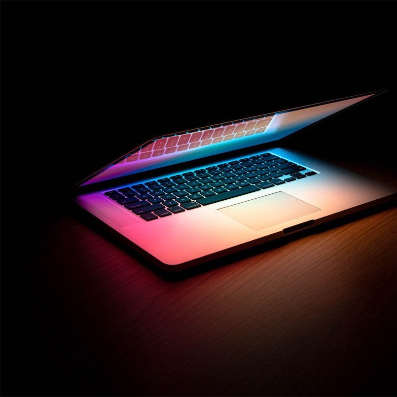 In einem dunklen Raum wird ein MacBook geöffnet, der dadurch bunte Lichter ausstrahlt