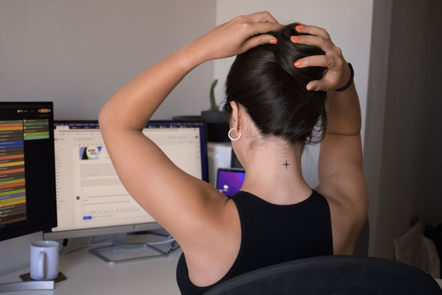 Eine Entwicklerin lehnt sich auf ihrem Stuhl zurück und macht ihre Haare, währenddessen ihr Computer weiterarbeitet.