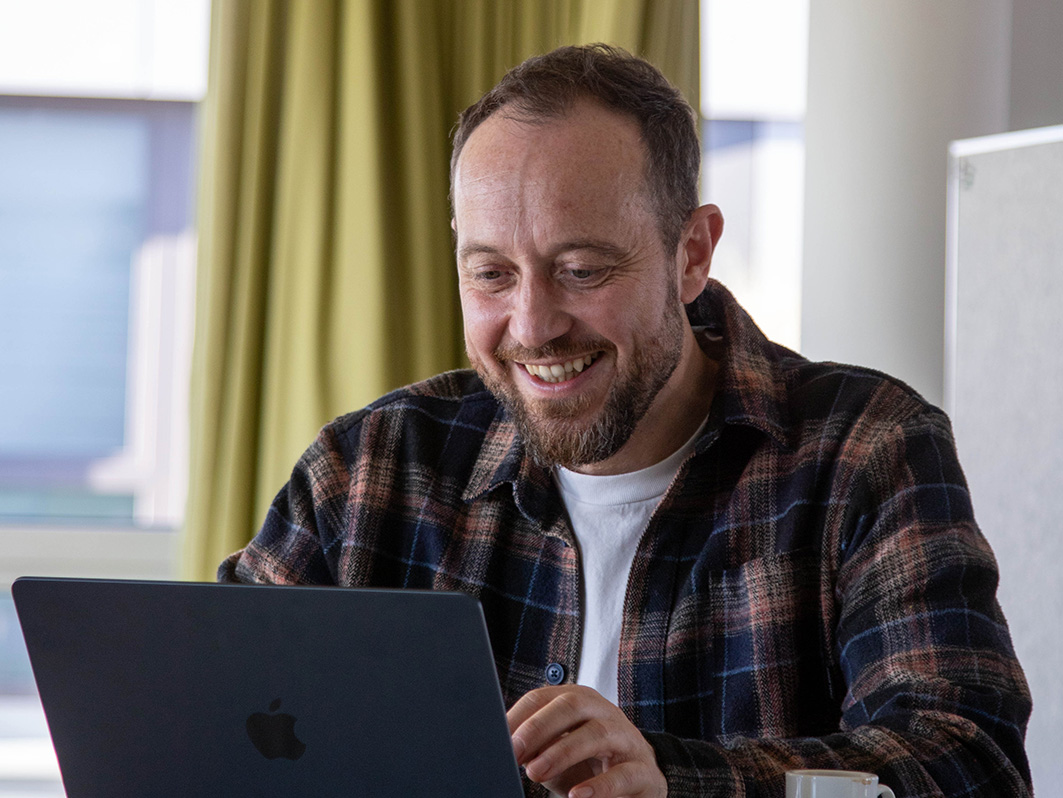 Daniel sitzt am Laptop und lächelt. 
