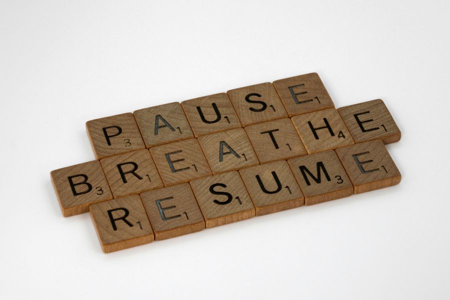 Pausieren und später fortsetzen Holzbuchstaben auf weißem Hintergrund bilden die Wörter „Pause“, „Breathe“ und „Resume“.
